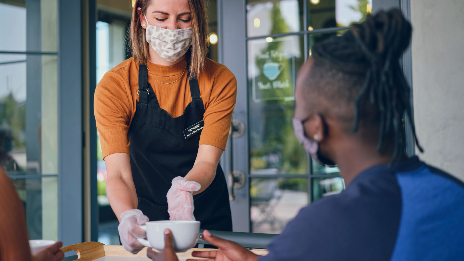 masked service employee serving a beverage to a customer